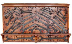 Una paret de fusta muntada amb una sèrie deines de ferro dèpoca, incloses diverses claus, alicates i martells, es mostra de manera organitzada. Les eines estan disposades en diagonal i espaiades uniformement, creant un patró visualment cridaner.