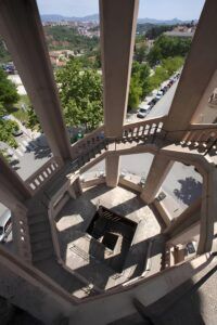 Vista des de dalt duna escala de cargol a Manresa, amb murs de formigó oberts que condueixen al carrer. Els arbres, els cotxes aparcats i els turons llunyans són visibles més enllà de lestructura arquitectònica.