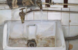A white ceramic sink with two brass faucets running water. The background features white tiled walls, and the sink shows signs of age with stains and tarnish. The scene has a vintage or rustic feel.