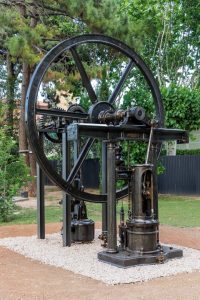 La màquina de vapor Alexander restaurada es mostra a l'exterior sobre un llit de grava blanca, envoltats d'arbres, vegetació al jardí del Museu de les Aigües